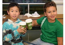 Two African Road Elementary students toast one another with paper cups of hot cocoa at the end of the Taste of A R E  event.