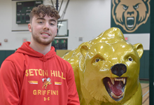 Aidan Brunetti, wearing a Seton Hill University red hoodie, stands next to the Vestal Golden Bear statute before his signing ceremony in the Vestal High School gym on January 28, 2022.