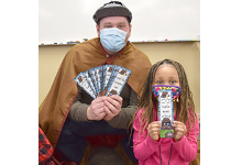 Sir Bookworm holds up a handful of Word Detective bookmarks along with a Clayton Avenue Elementary first-grade girl who is holding her bookmark.