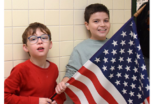 Two Tioga Hills Elementary students hold a large flag as they stand in the hallway to welcome local veterans on November 9, 2023.