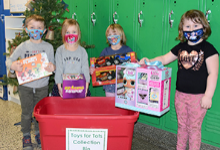 Four Universal Pre-Kindergarten students at the Cub Care campus stand by a red bin with toys they are about to put into it.