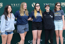 Five Vestal High School seniors, four girls and one non-binary, in front of the green and tan Vestal Golden Bear wall.