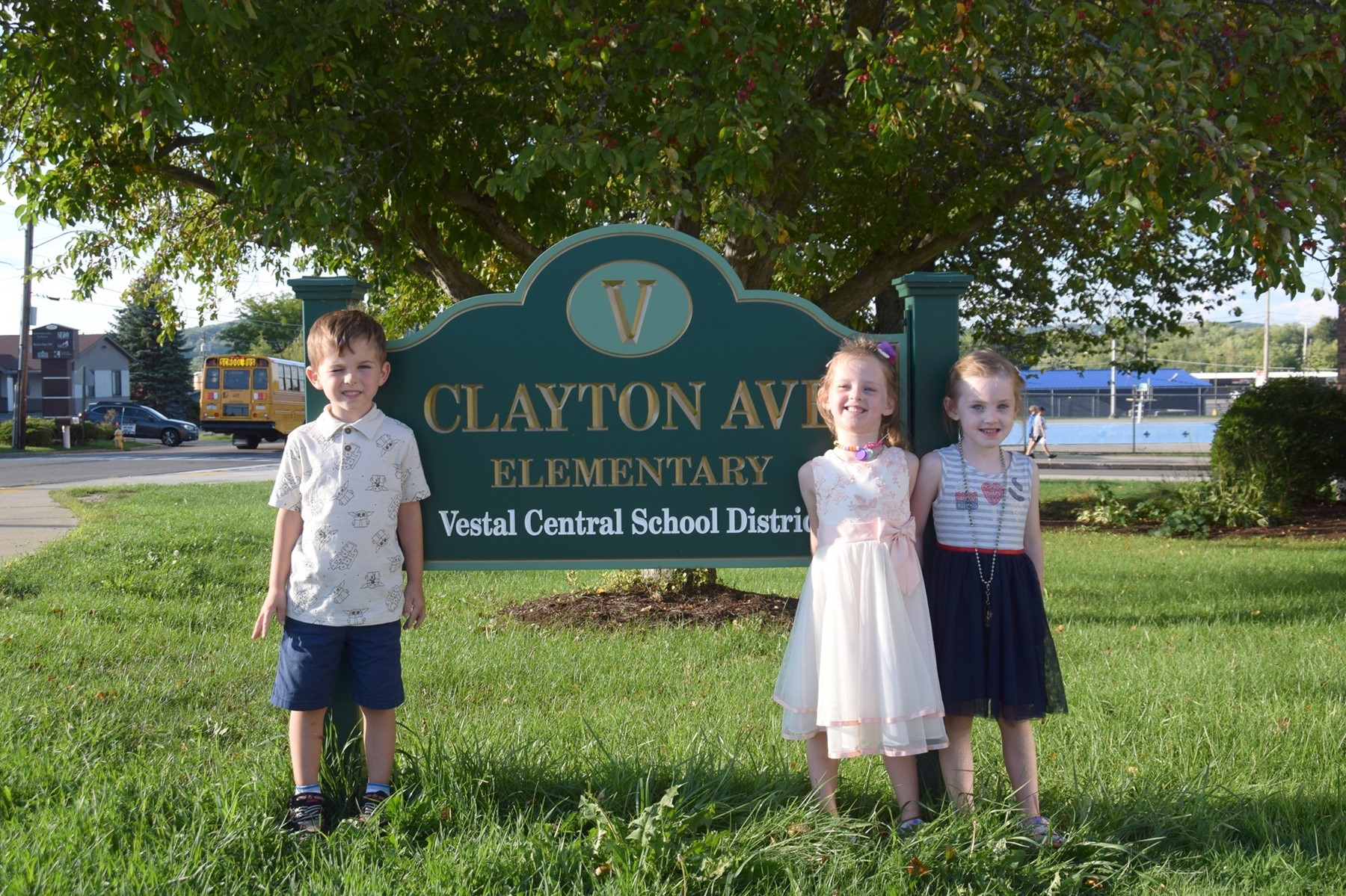Three Clayton Avenue Elementary Kindergarten students, a boy and two girls, flank the sign outside the building during Kindergarten Orientation.