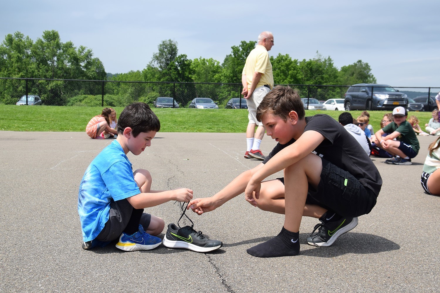 A fifth-grade boy patiently shows a Kindergarten boy how to tie his shoes on June 16, 2022.