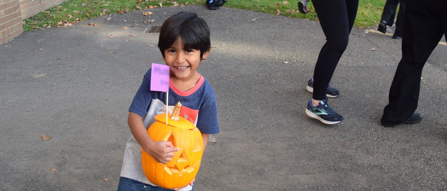 A small Universal Pre-Kindergarten student holds his carved pumpkin.