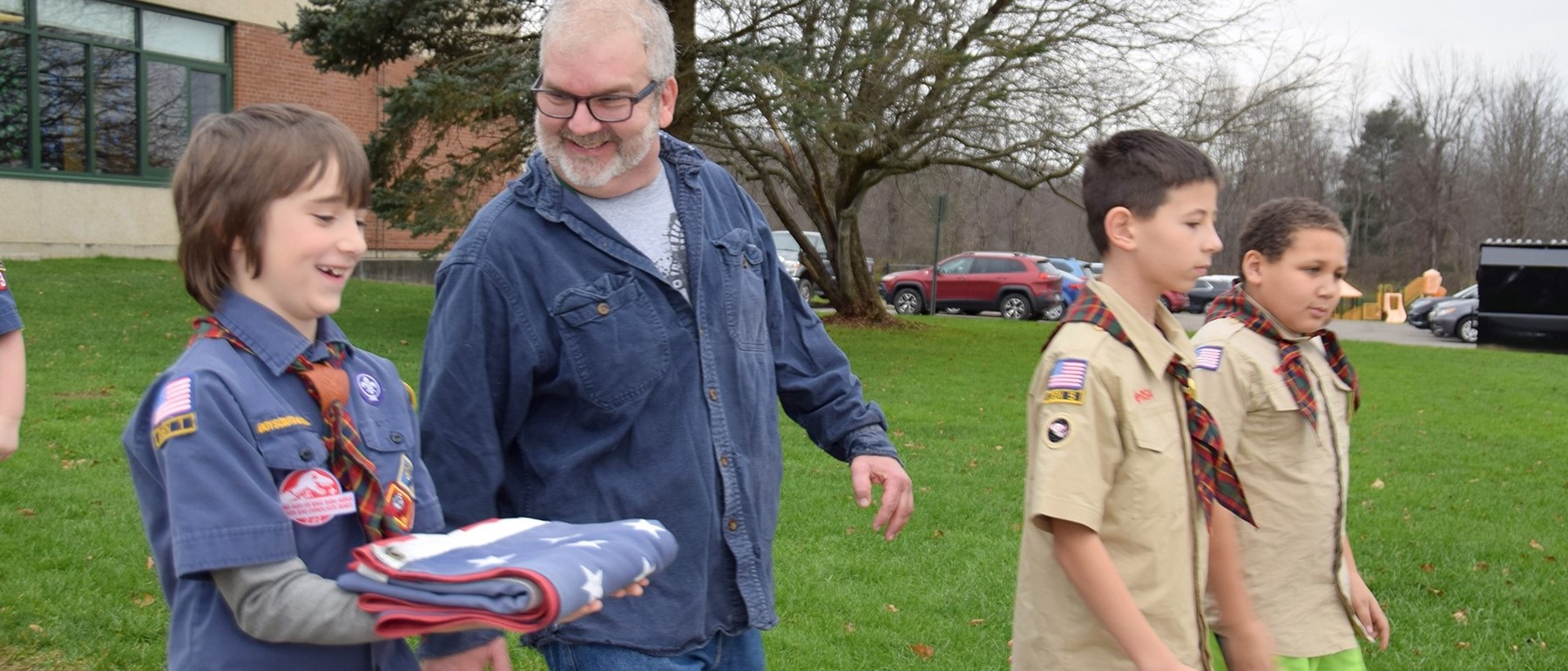 A Tioga Hills Elementary student wearing his Cub Scout uniform carries the flag out to the flagpole with Mr. Doolittle, head custodian.