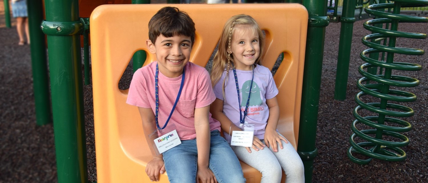 Two African Road Elementary Kindergarten students  sit on a bench together on the playground during Kindergarten Orientation on August 31, 2023.