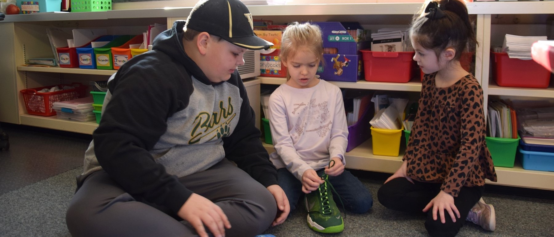 A Tioga Hills fifth-grader helps two Kindergarten students learn how to tie their shoelaces.